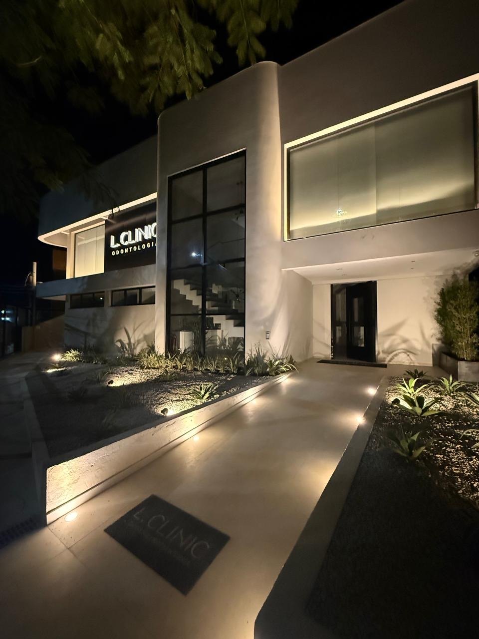 Entrada da clínica iluminada à noite, com caminho de pedra e jardim